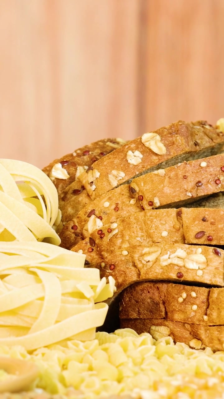Whole grain bread and pasta arranged with various grains on a wooden surface. Warm lighting enhances the natural textures