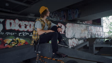 calm teenager relaxing on ramp at skatepark. handsome man having break.