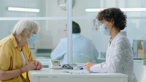 doctor in mask taking temperature of senior woman