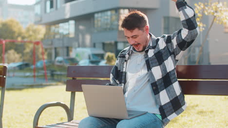 feliz hombre maduro trabajando en una computadora portátil netbook gritando de alegría en un banco en el centro de la ciudad