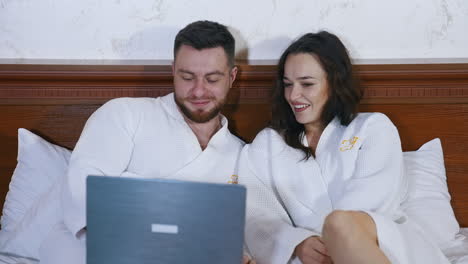 beautiful couple in love sitting on bed and watching movie on laptop. happy holidays of a young man and woman. vacation and honeymoon concept.