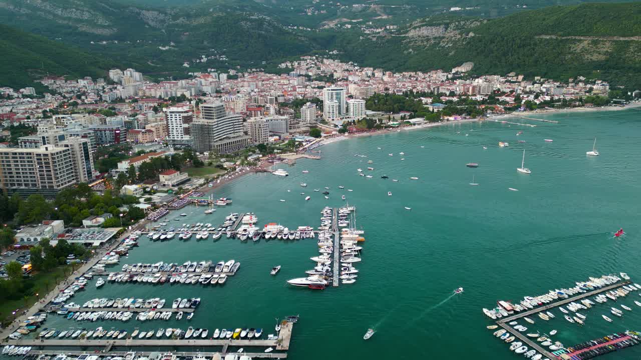 City of Budva, perspective from above. Drone passing forward above the port area of the city. Luxury yachts and boats docked. Famous travel destination in Montenegro. Blue hour, street light on.