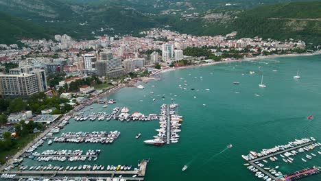 city of budva, perspective from above. drone passing forward above the port area of the city. luxury yachts and boats docked. famous travel destination in montenegro. blue hour, street light on.