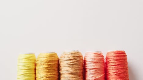 video of five reels of yellow to orange embroidery threads on white background with copy space