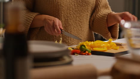 close up of woman at home in kitchen preparing healthy fresh vegetables for vegetarian or vegan meal slicing red and yellow peppers on board