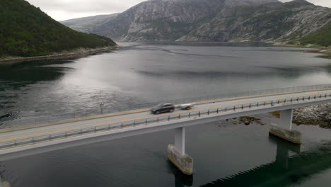 aerial shot of a bridge as a car drives over with lake and mountain backdrop, norway