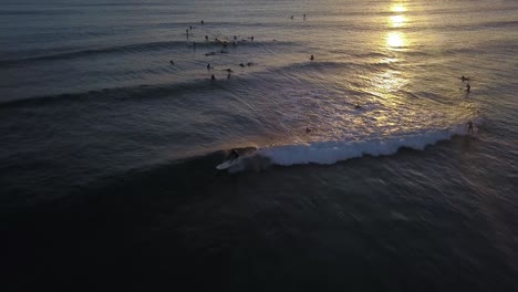 Surfer-catching-a-wave-in-the-reflective-golden-glow-of-sunset,-Hawaii