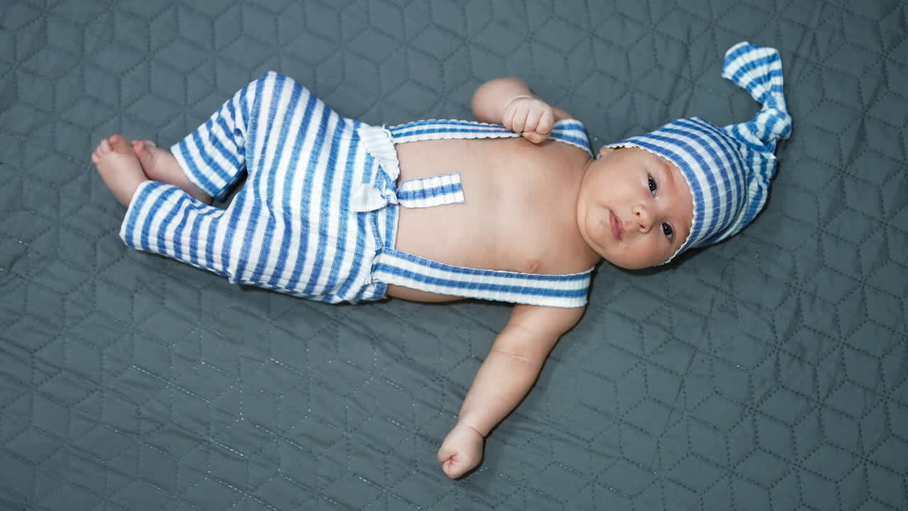 Tiny toddler resting on the bed. Baby boy wearing adorable funny outfit close up. Grey blanket background.