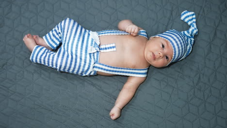 tiny toddler resting on the bed. baby boy wearing adorable funny outfit close up. grey blanket background.
