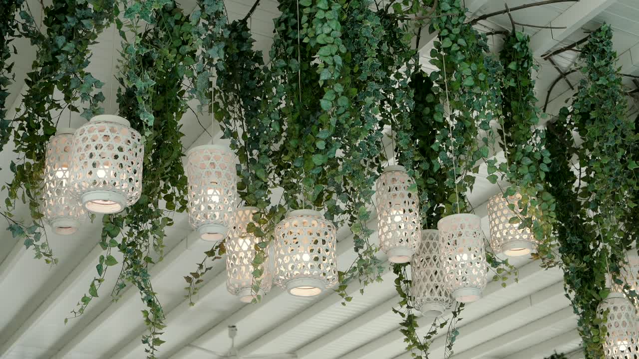 Wicker pendant lamps and green vines hanging from a white outdoor ceiling