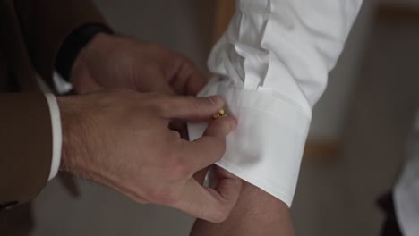 close up of hands fastening a gold cufflink on a white shirt sleeve