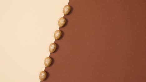 el concepto de colocación plana mínima de huevos de oro rotativos de brillo de pascua en un fondo marrón desnudo.