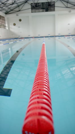 vertical video: empty indoor swimming pool with red lane divider stretching into distance