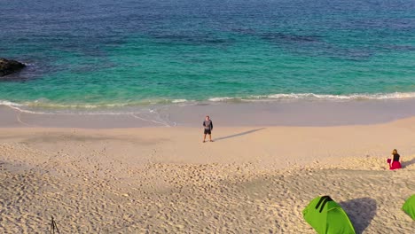 caucasian man flying drone on beach in oman, aerial dolly out
