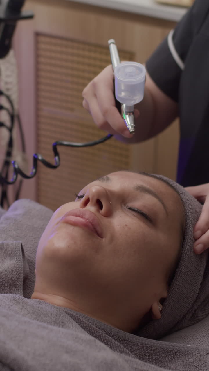 Vertical of Esthetician Spraying Moisturizing Equipment on Face of Woman