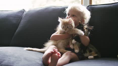 a little girl sitting on the couch holding two kittens