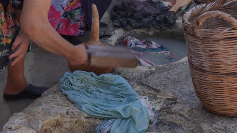 primer plano de una mujer usando una herramienta de madera para golpear su ropa durante una recreación histórica del lavado de ropa como lo hacían en el siglo xx en kritou terra, grecia.