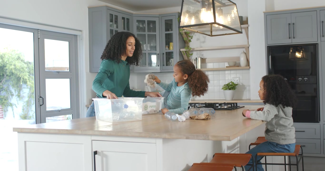 Madre e figli afroamericani che smistano bottiglie di plastica in cucina per riciclare dopo averle posizionate
