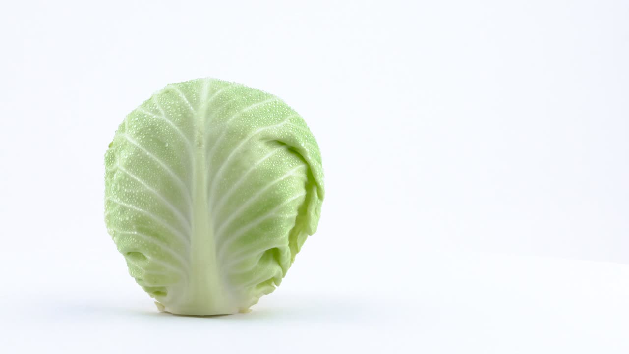 la mitad del marco de un mini repollo blanco entero con gotas de agua está girando en la mesa giratoria aislada en el fondo blanco. primer plano. macro.