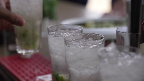 bartender preparing several iced cocktails in a row with a mixing spoon