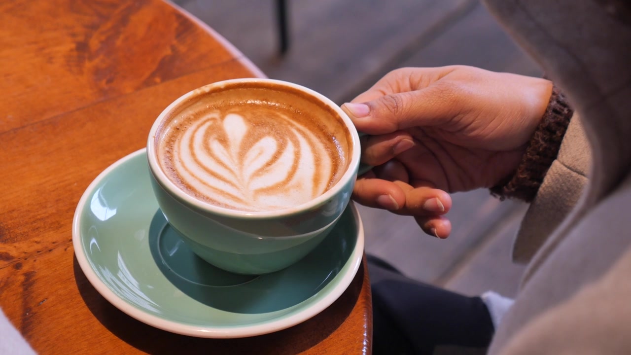 Persona che tiene una tazza di latte macchiato con latte art a forma di cuore