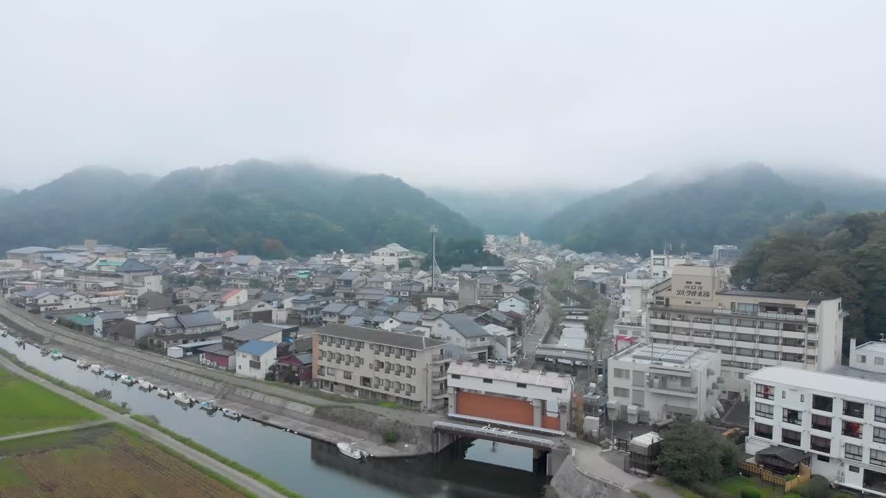 Early morning aerial shot of Kinosaki Onsen, famous small hot spring town in Hyogo prefecture, forward and pan motion revealing the famous canal, with epic cloud covered mountains in background