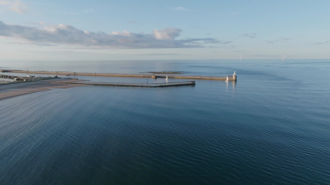 Wide angle static drone clip showing curving water currents around harbour walls towards beach