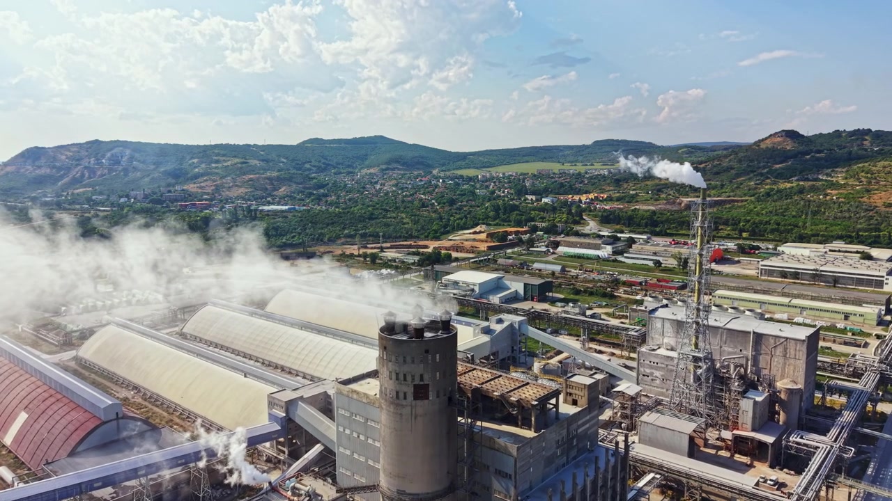Industrial site with buildings, smoke stacks, and machinery in a rural area during daylight hours