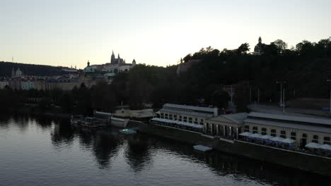 Rising-aerial-of-restaurant-by-water-in-Prague-and-distant-castle