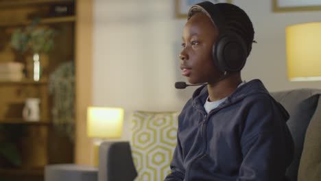 boy at home sitting on sofa wearing headset playing video game 3