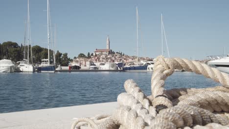 Nahaufnahme-Eines-Schiffsseils,-Das-Auf-Dem-Boden-Liegt,-Mit-Luxusbooten-Und-Der-Insel-Rovinj-Im-Hintergrund