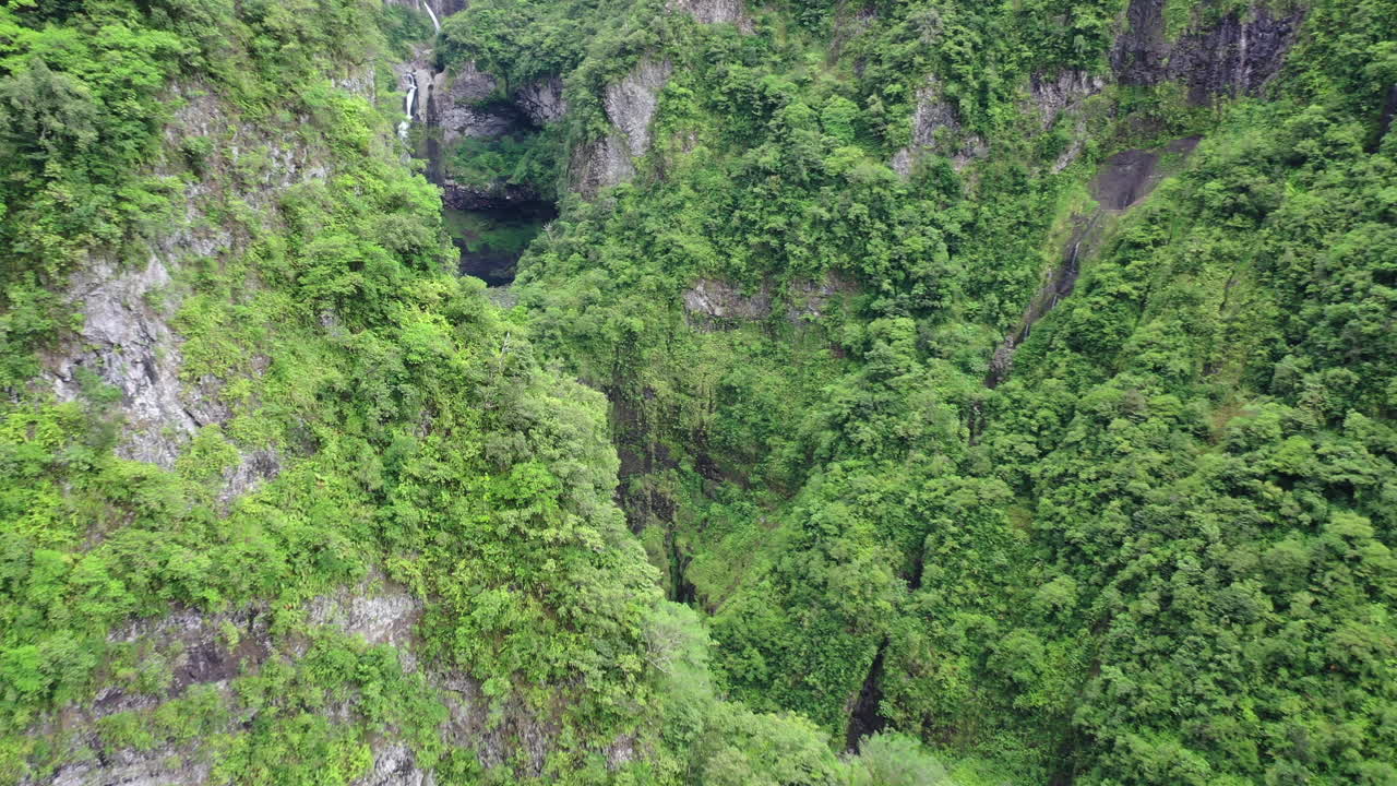 vuelo aéreo sobre montañas cubiertas de vegetación para revelar las cascadas de takamaka en la isla de la reunión