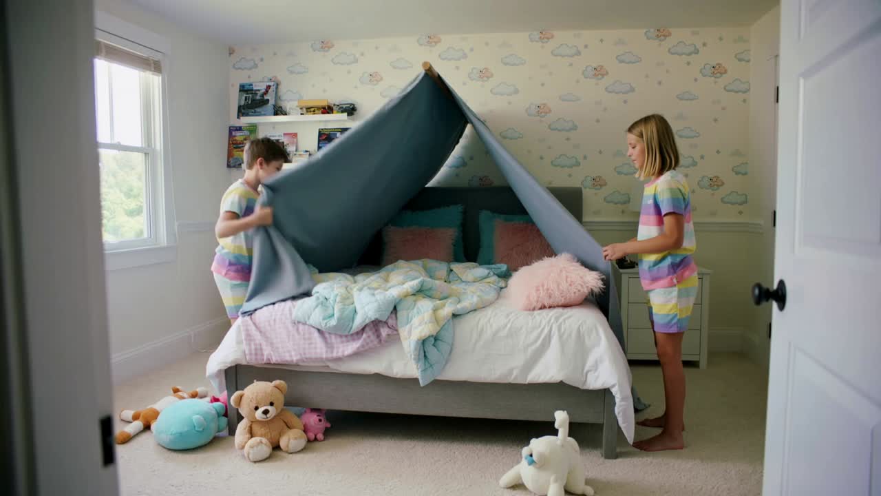 Lifting gray blanket, siblings in striped pjs forming fort in bedroom, placing pink pillow for play