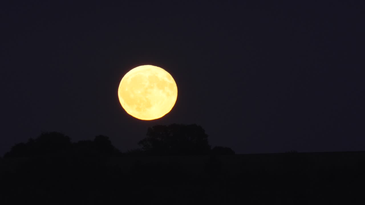 Lua cheia surge sobre colinas escuras contra o céu noturno. Time-lapse