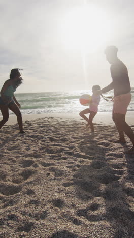 video vertical de una feliz familia biracial jugando en una playa soleada