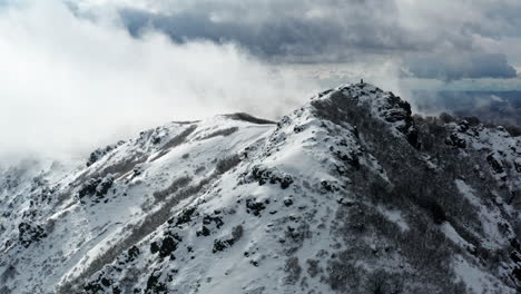 Snow-capped-mountain-peaks-shrouded-in-clouds,-aerial-shot-capturing-rugged-terrain-and-serene-landscape