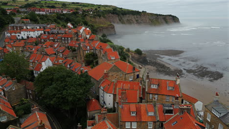 pullback establishing aerial drone shot of robin hood's bay on misty morning at low tide