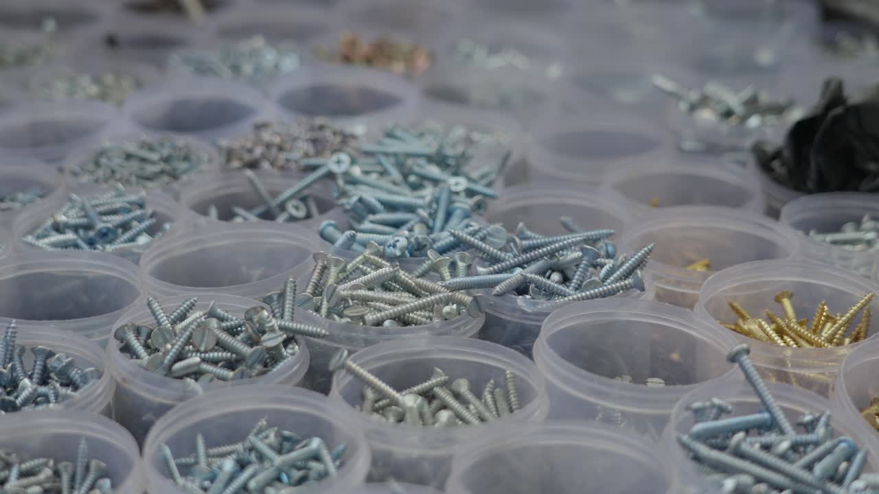 Primo piano di varie viti e bulloni metallici di diversi colori organizzati in piccoli barattoli di plastica presso una bancarella di ferramenta in India. Ideale per concetti di edilizia, fai da te e forniture industriali.