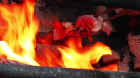 bacon being cookend on outdoors barbecue with huge yellow-red flame and heat while grease are going down to the flame