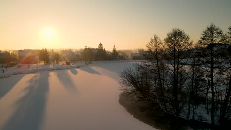 Aerial-backwards-flight-over-snow-covered-Lake-and-city-silhouette-with-sunrise-in-background