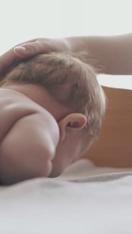 cute restless newborn boy cries lying on stomach during massage and mother pets baby short haired head close view