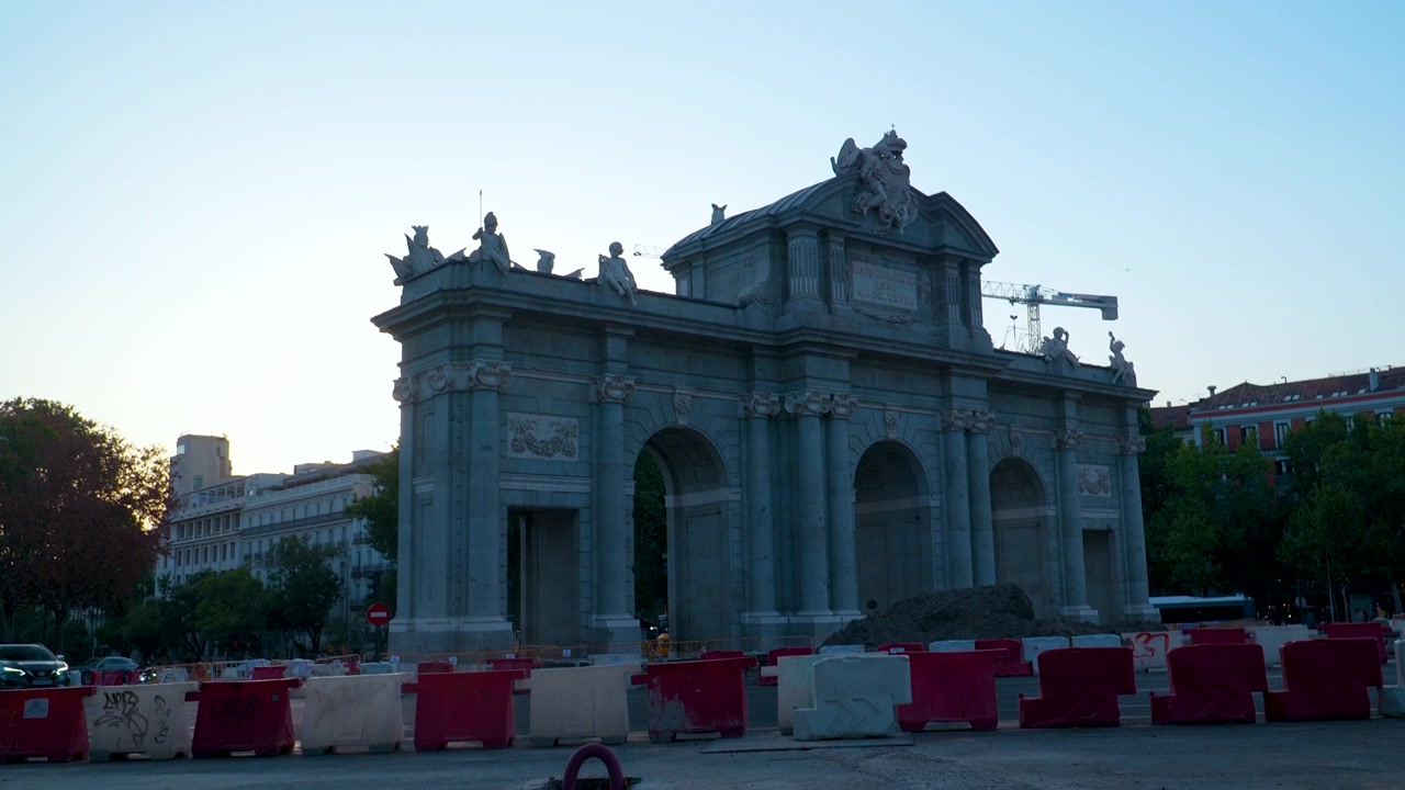 Uma tomada ampla do histórico arco do triunfo Puerta de Alcalá em Madrid, Espanha, capturada durante a hora dourada do início da manhã com barreiras de construção da cidade em primeiro plano