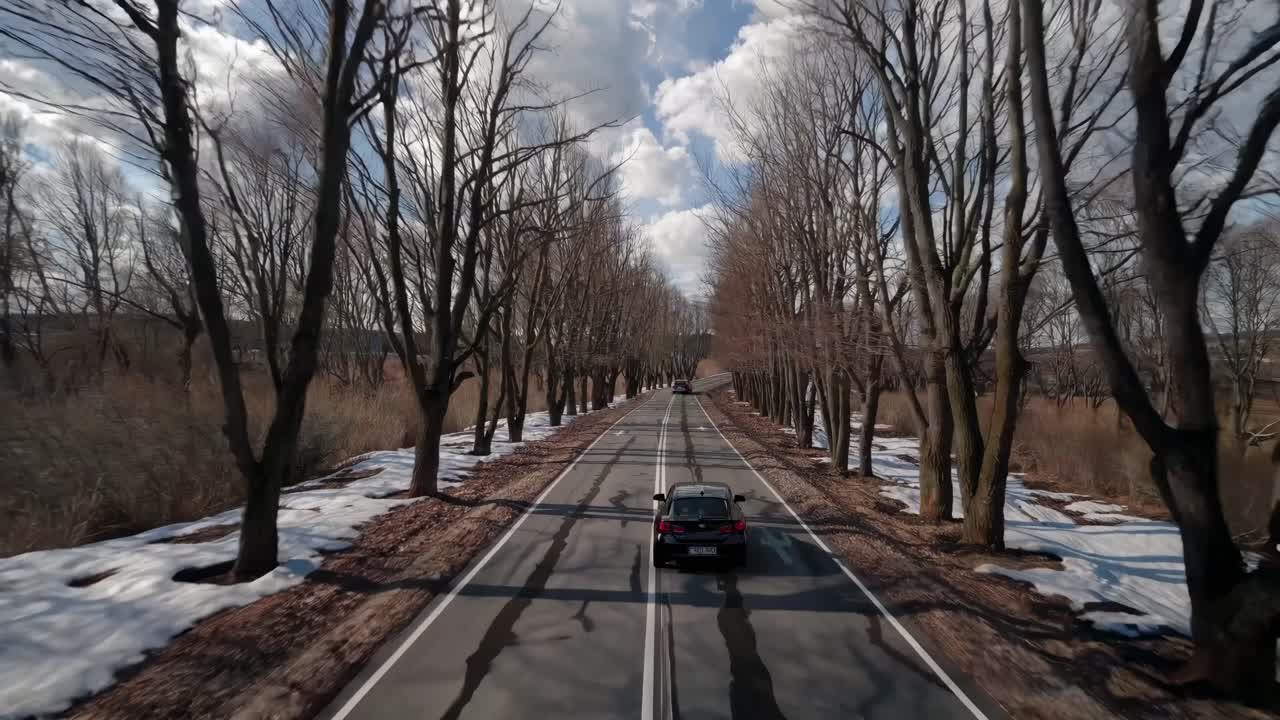 Aerial video of a car driving on a snowy, tree-lined road, showcasing a serene winter landscape