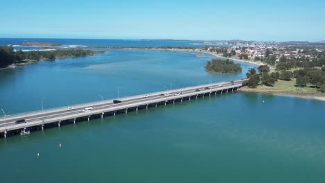 Windang-Bridge-over-estuary-connecting-Lake-Illawarra-to-Pacific-Ocean-on-sunny-day,-aerial