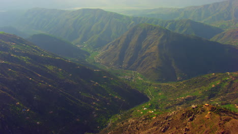 Blick-Auf-Die-Berglandschaft-Mit-Drohne,-Große-Grüne-Bergserie-Mit-Häusern,-Luftflug-über-Die-Berge,-Kameraobjektiv-Ist-Durch-Den-Wind-Etwas-Laut