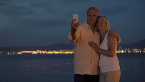 Pareja-Mayor-De-Vacaciones-Tomando-Selfie-Celular-Por-La-Noche