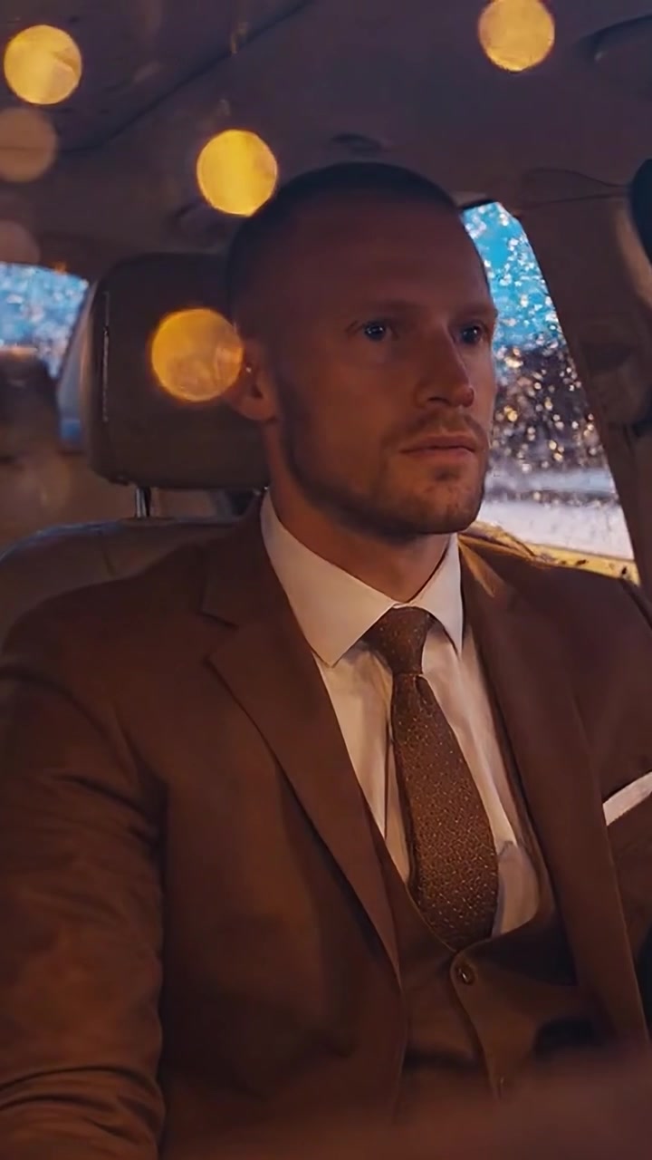 Un uomo contemplativo in abito formale che osserva l'ambiente circostante mentre è seduto in un'auto durante una sera piovosa, mostrando emozioni di serietà e profondità.