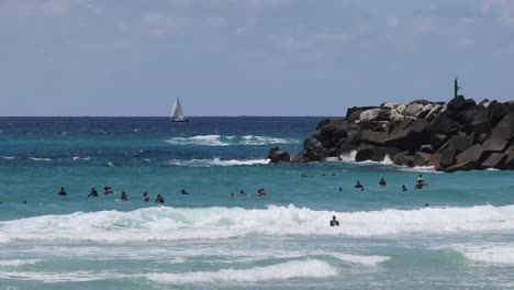 crowded beach scene with surfers and sailboats