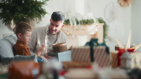 little boy and his dad sit on the couch and talk during christmas