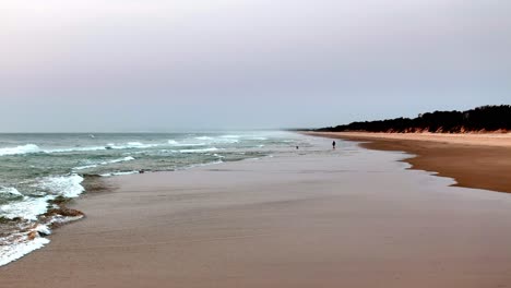 Serenidad-Crepuscular-En-Una-Playa-Apartada:-Suaves-Olas-Rompiendo-La-Orilla-Arenosa-Mientras-Cae-El-Atardecer